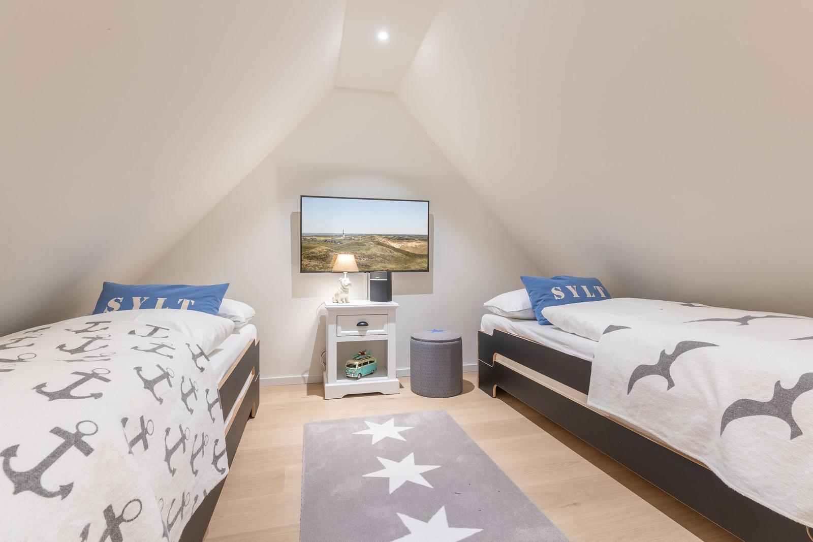 Two single beds with Sylt bedding, TV, and small nightstand.