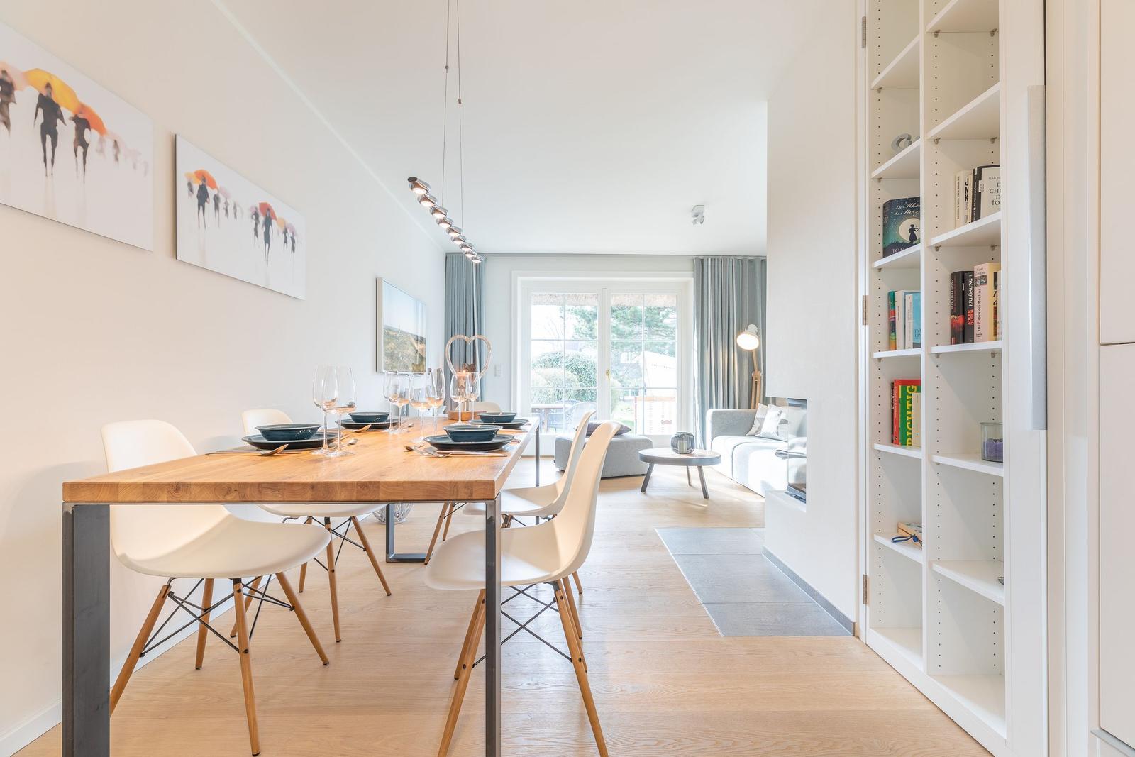 Dining area with table and chairs, view into living room with sofa and bookcase.