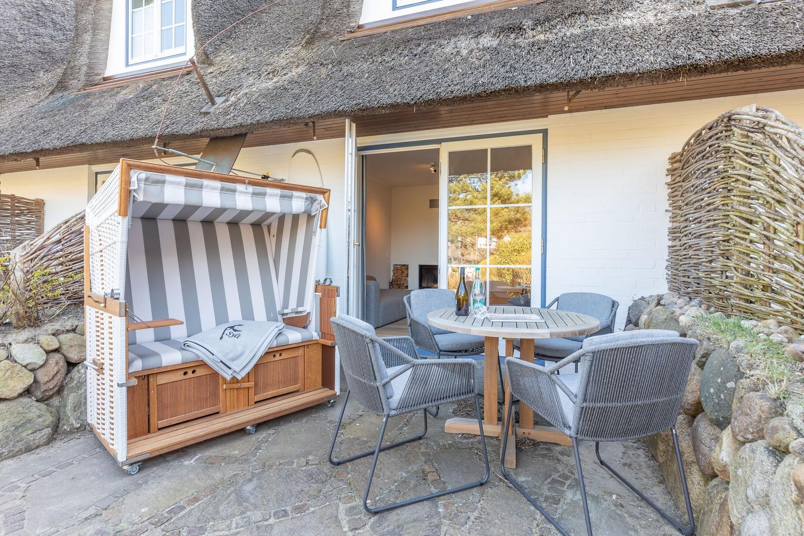 Terrace with beach chair, table and chairs in front of a house with thatched roof.