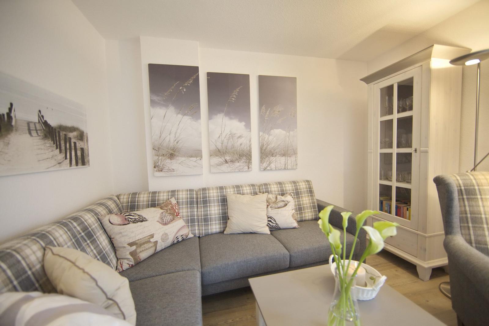 Living room with sofa, cushions, and glass cabinet. Wall art shows beach motif.