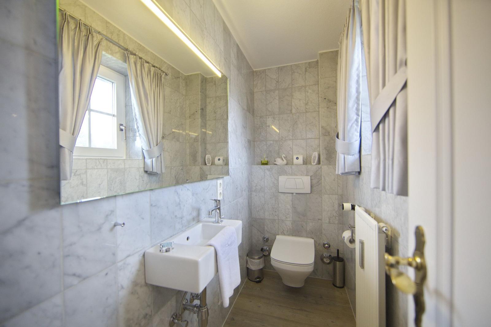 Bathroom with sink, toilet, and mirror. Tiled wall and window with curtains.