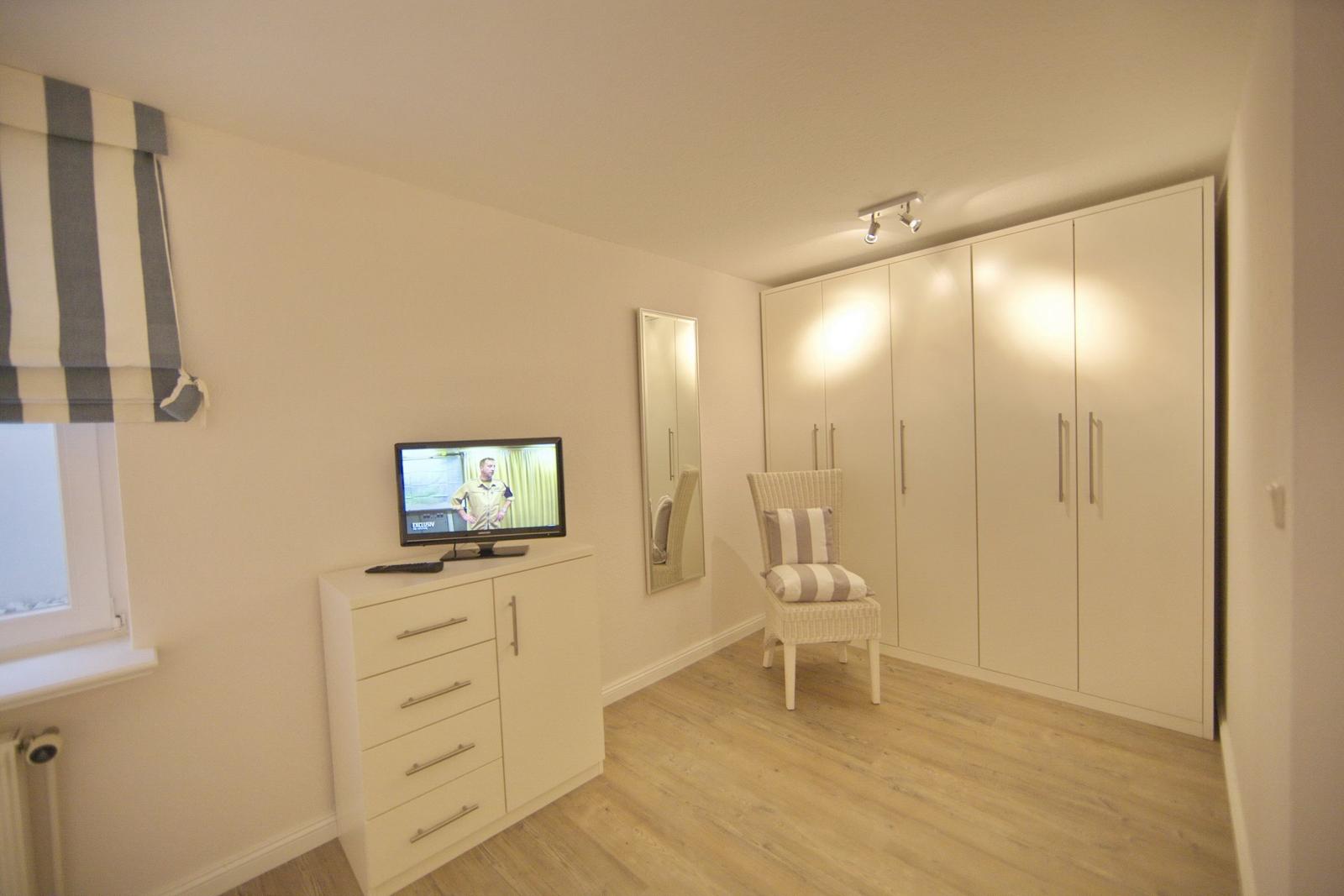 Bedroom with wardrobe, chair, and TV on cabinet.