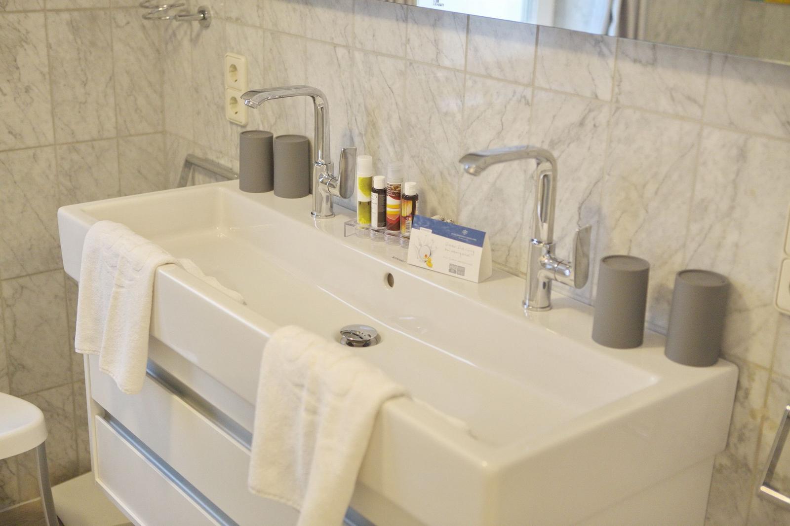 Bathroom with sink, two faucets, and gray containers.