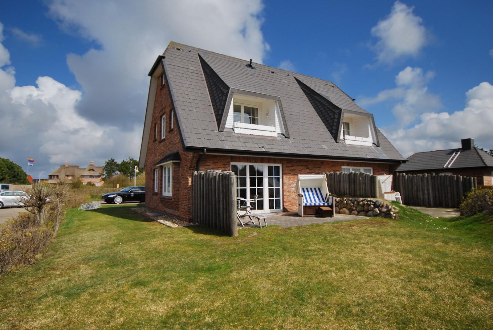 A house with red brick, gray roof, and terrace with lounge chair.
