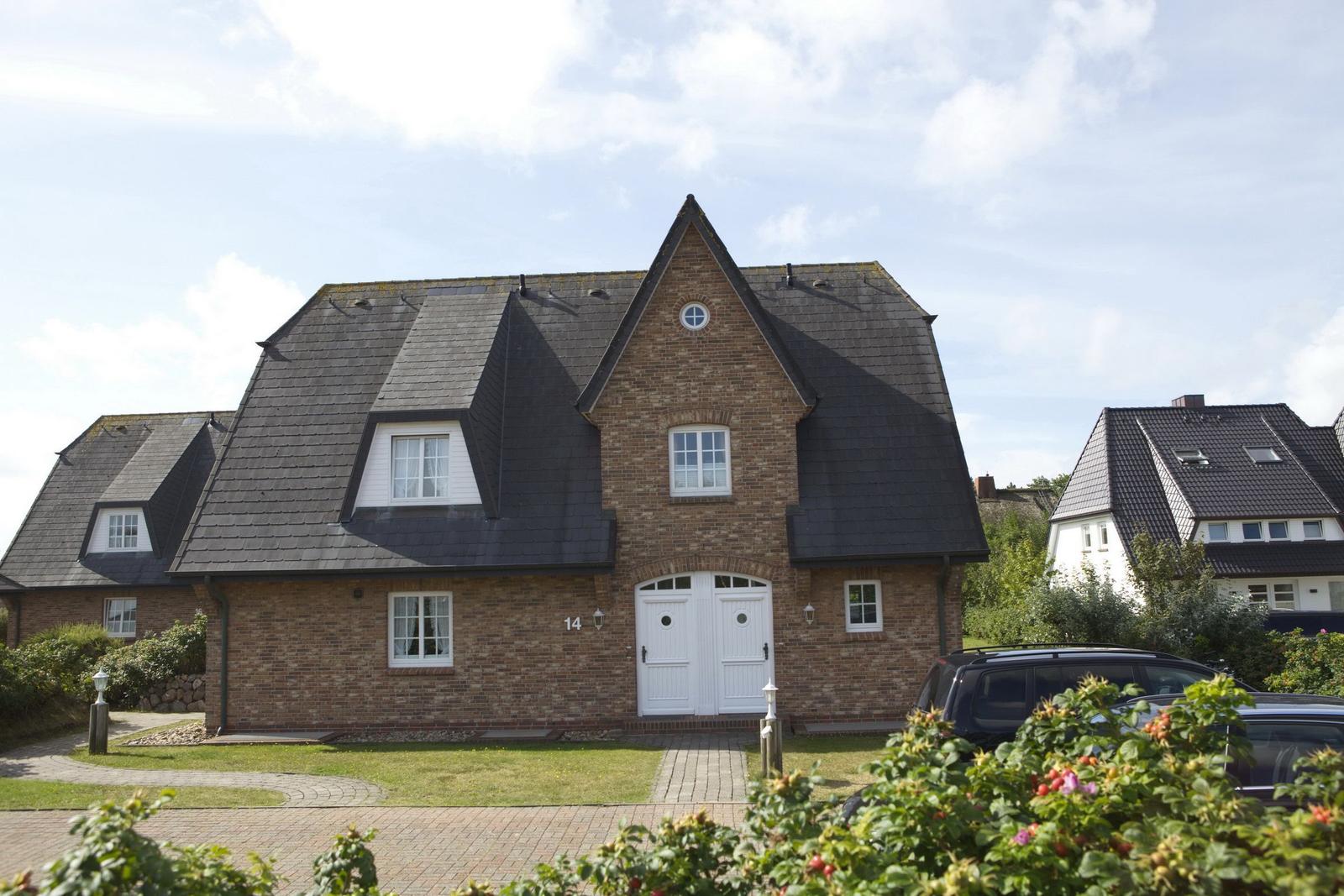 House with brick facade, dark roof, and white door. Number 14. Lawns and paved paths.