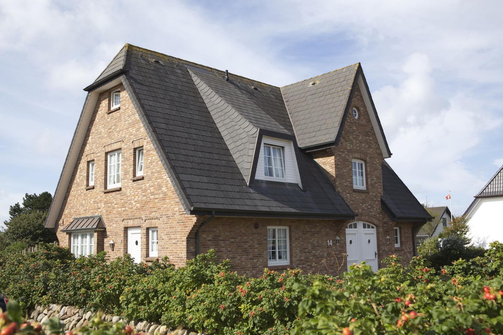 Two-story brick house with dark roof and white windows. Front garden with rose hedge.