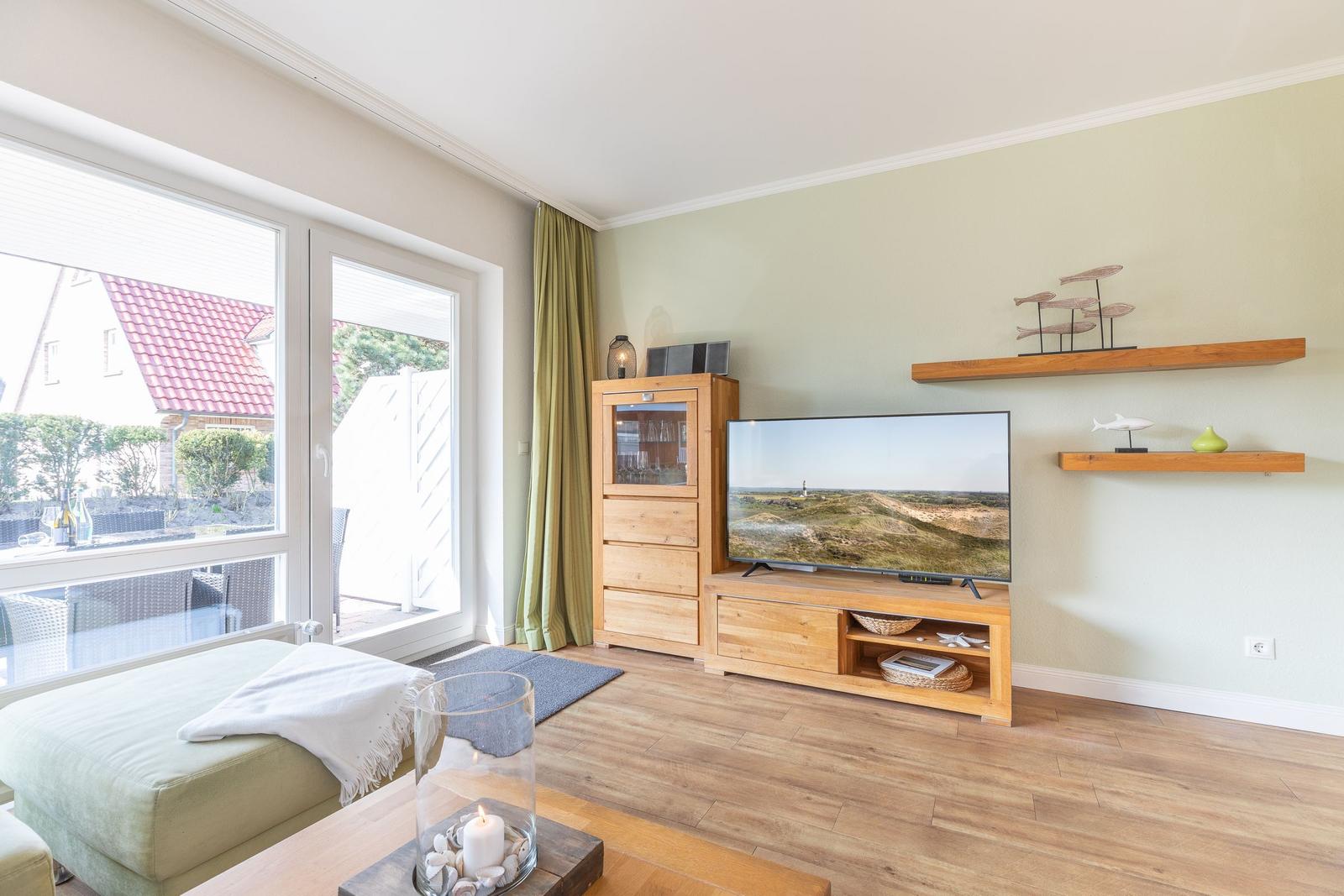 Wohnzimmer mit Fernseher, Holzmöbeln und Blick auf Terrasse.