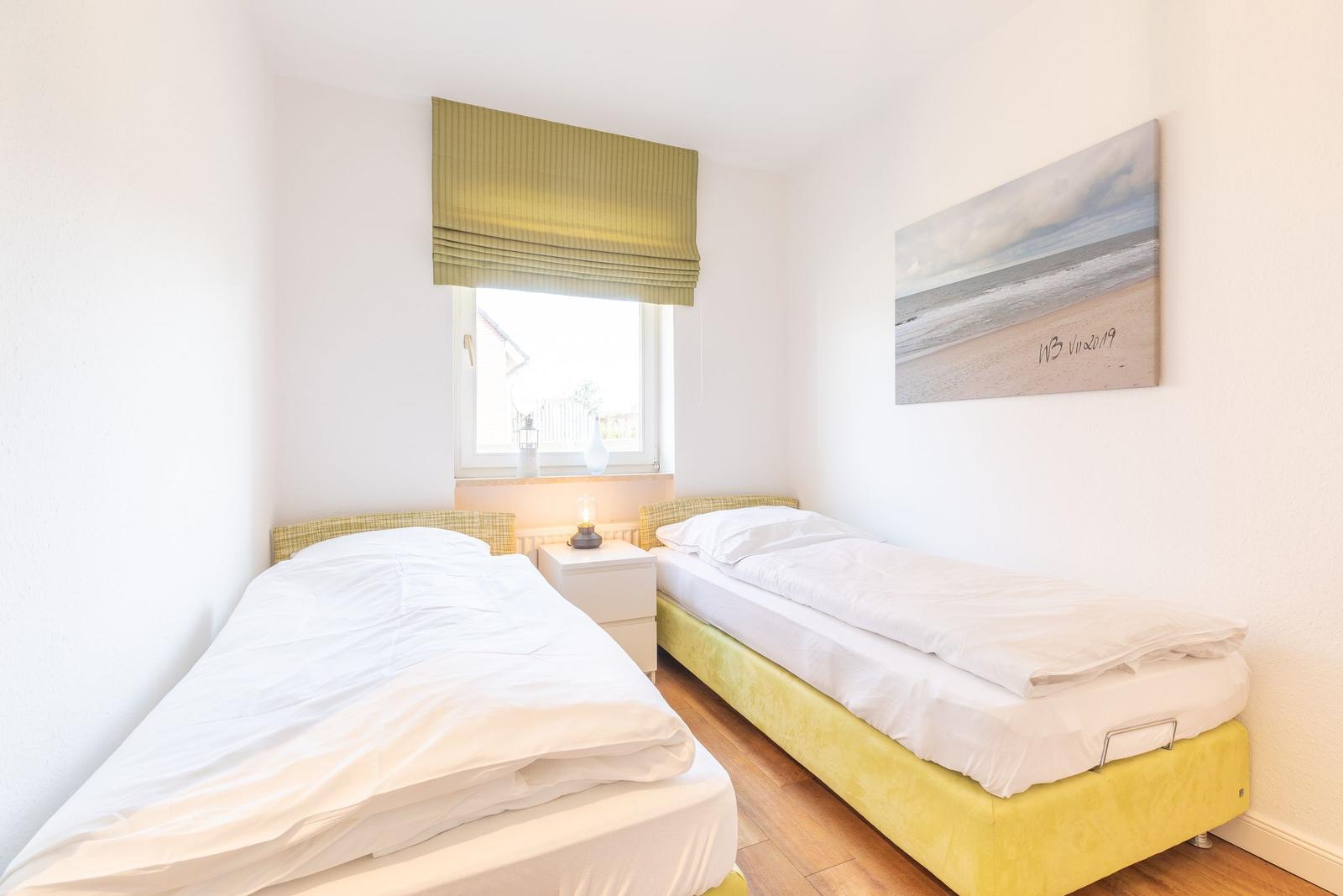 Zwei Einzelbetten mit weißen Bettwäsche, Fenster mit grünem Rollladen und Wandbild.