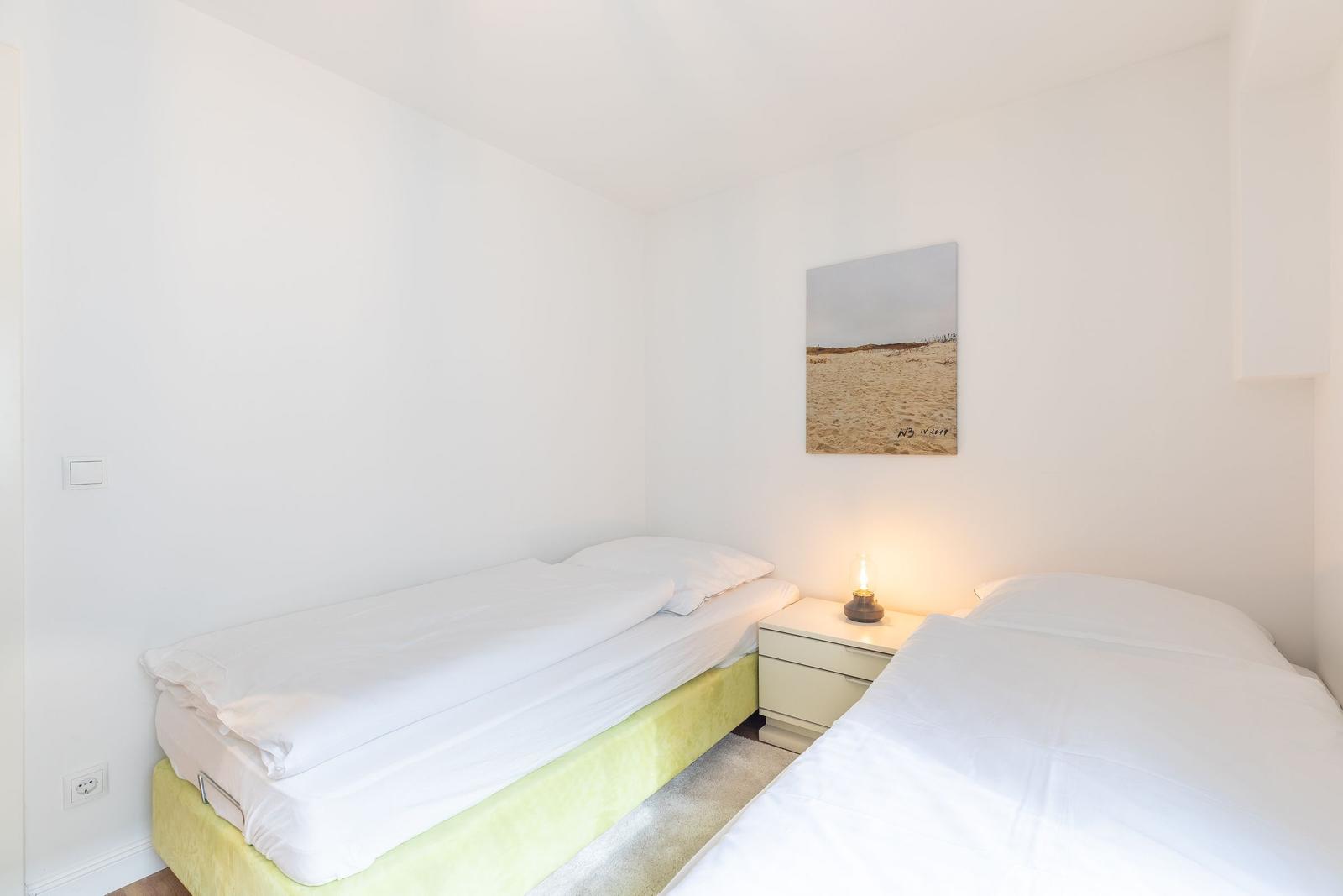 Zwei Betten mit weißen Laken, Nachttisch mit Lampe und Wandbild.
