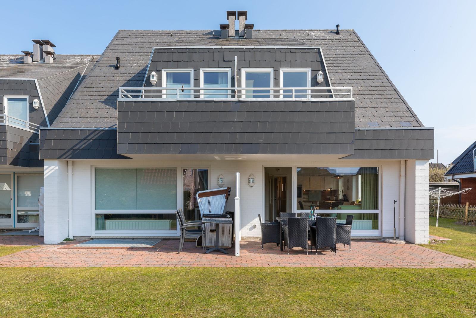 Haus mit Balkon, Terrasse und Gartenbereich mit Sitzgelegenheiten.