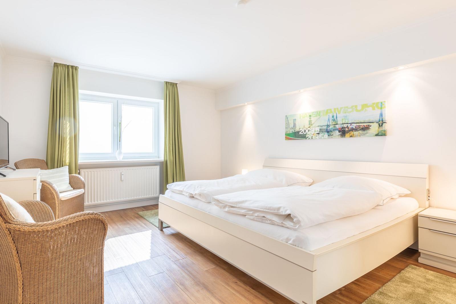 Ein Schlafzimmer mit Doppelbett, Fenster, grünen Vorhängen und Wandbild.
