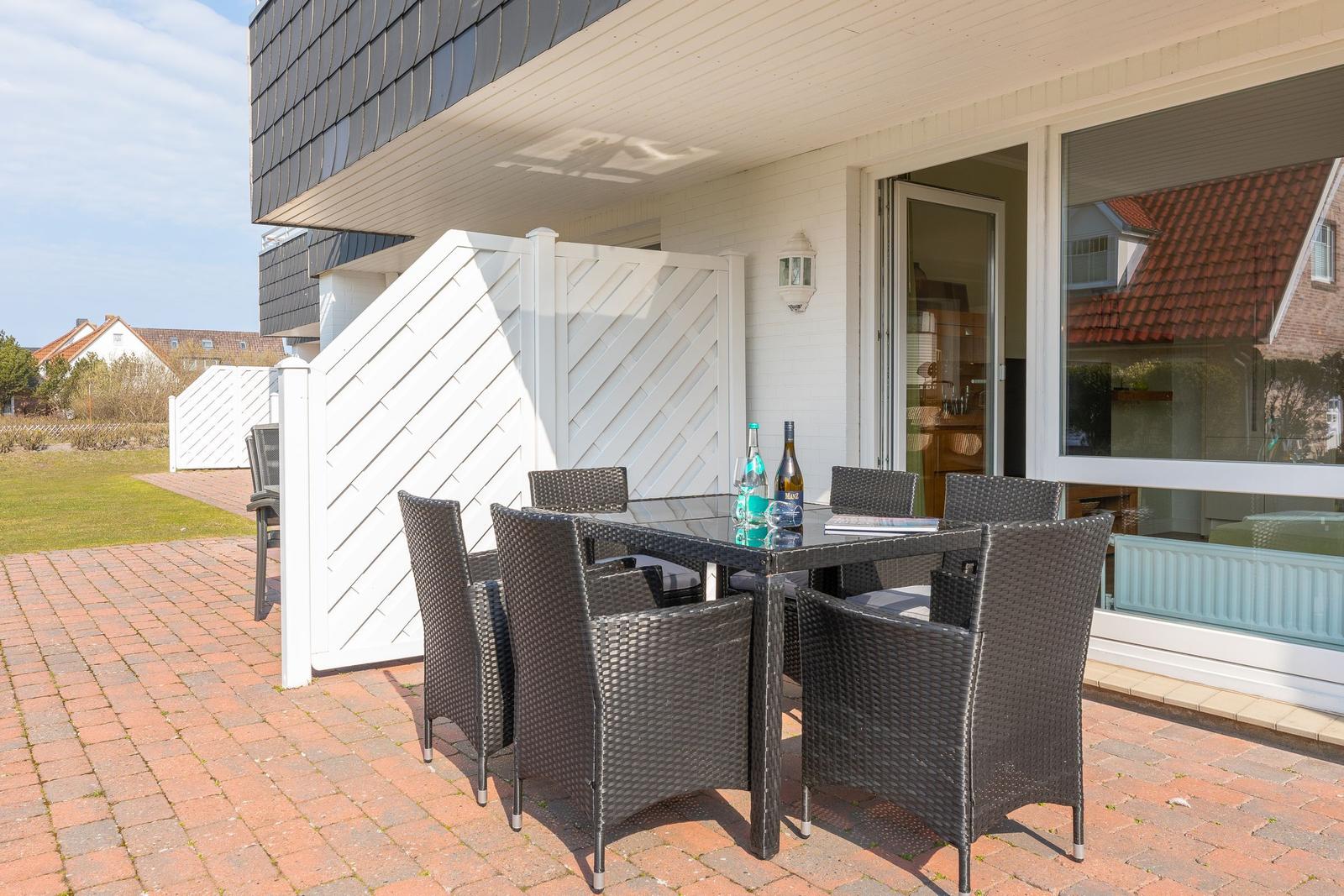 Terrasse mit Gartentisch und sechs Stühlen, umgeben von weißem Zaun und rotem Pflaster.