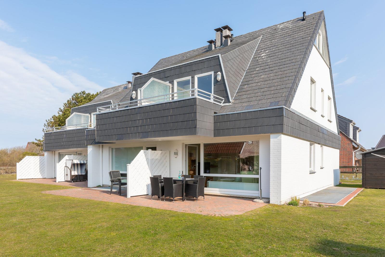 Moderne Villa mit Balkon, Terrasse und Garten. Große Fenster und schwarz-weiße Fassade.