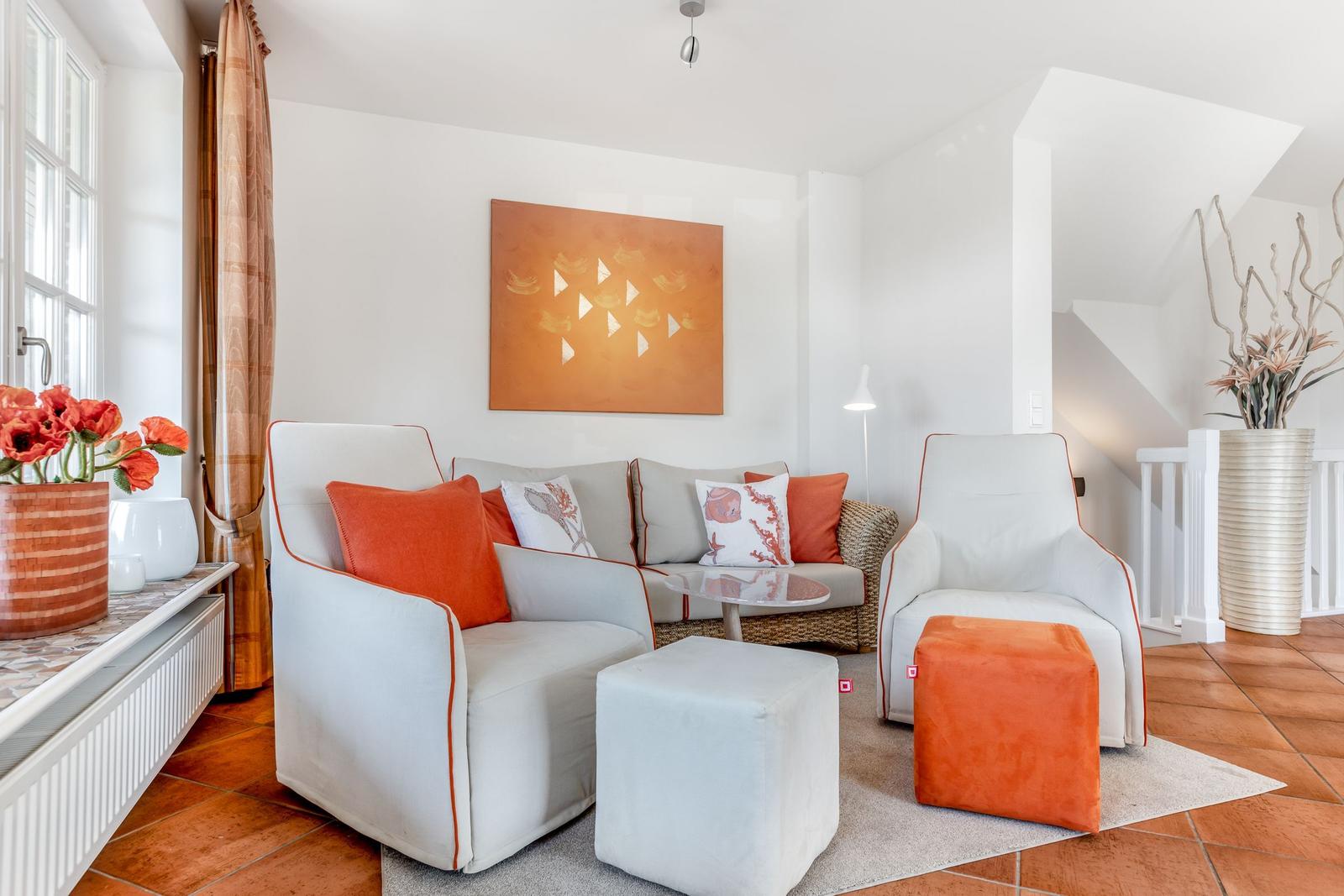Living room with white sofa, orange cushions and ottomans. Wall art and plants complete the space.