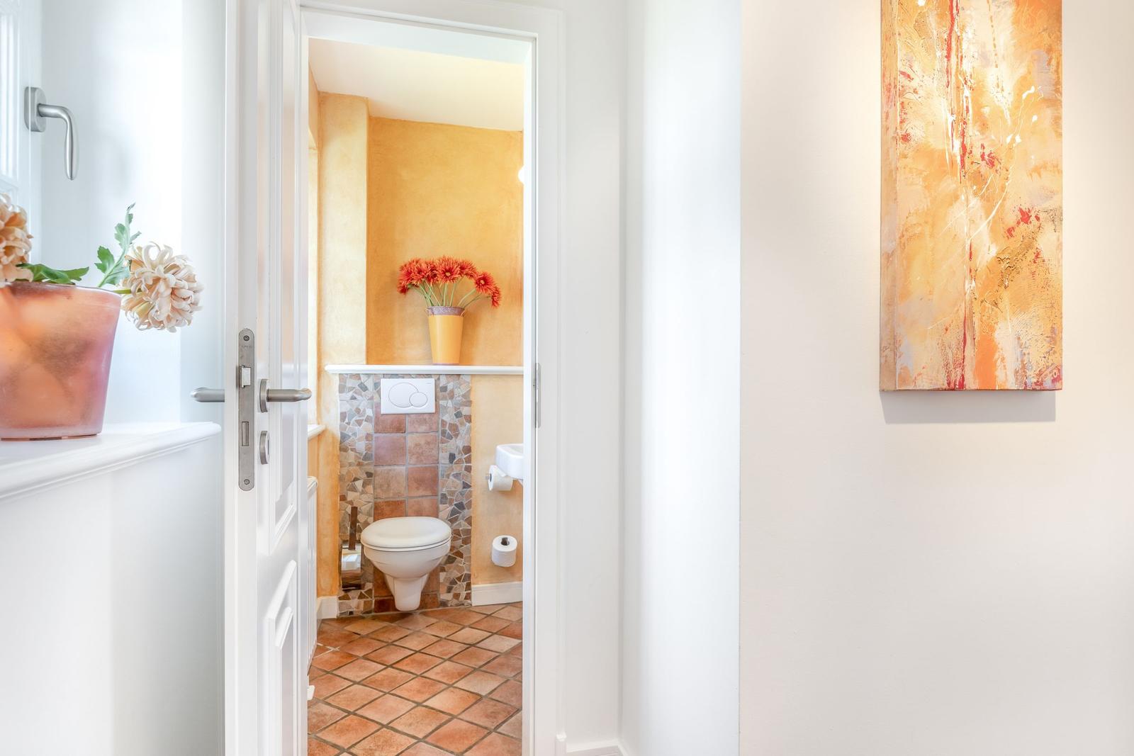 Bathroom with toilet, mosaic wall, and flowers