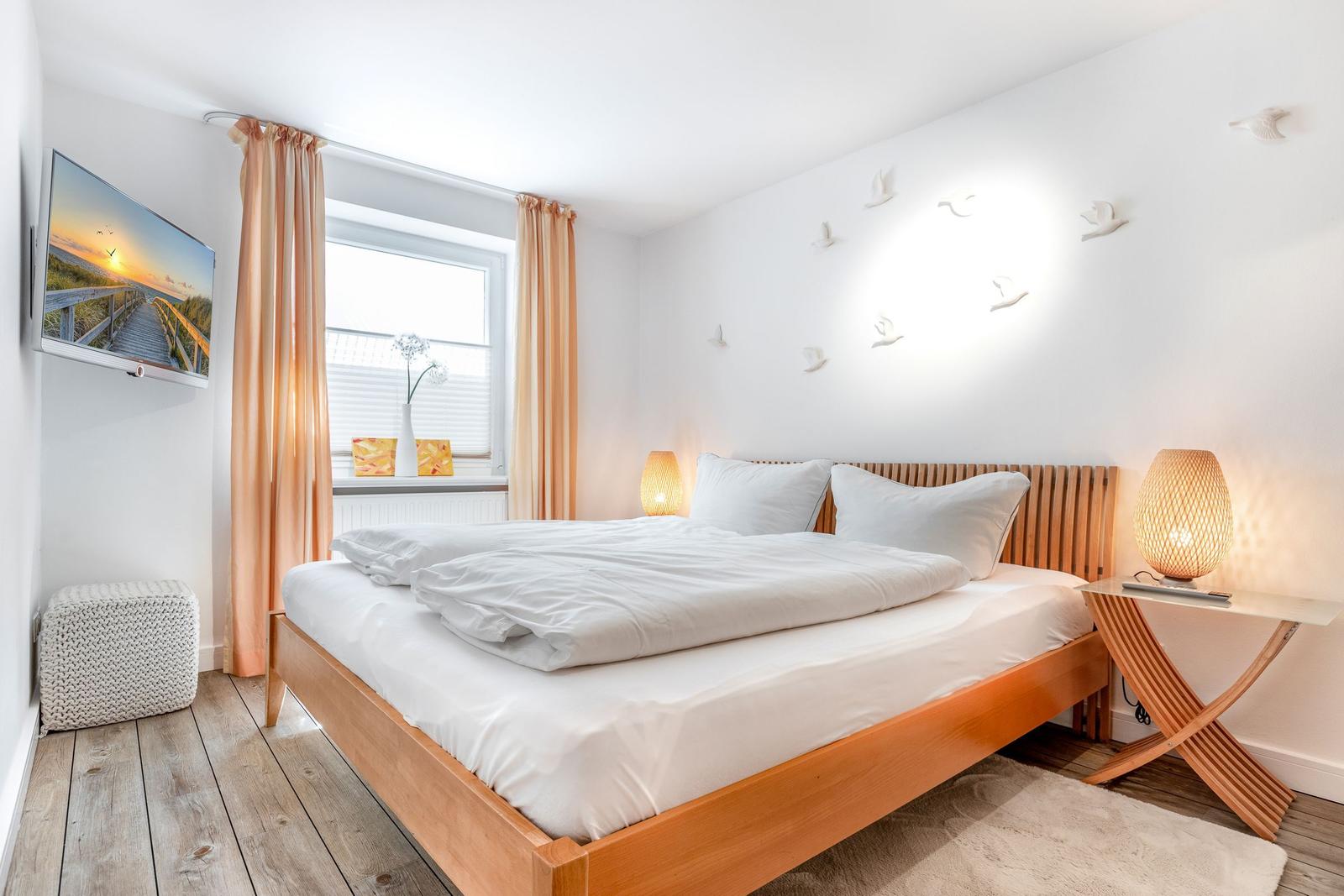 Bedroom with wooden bed, window, TV, and nightstand with lamp.