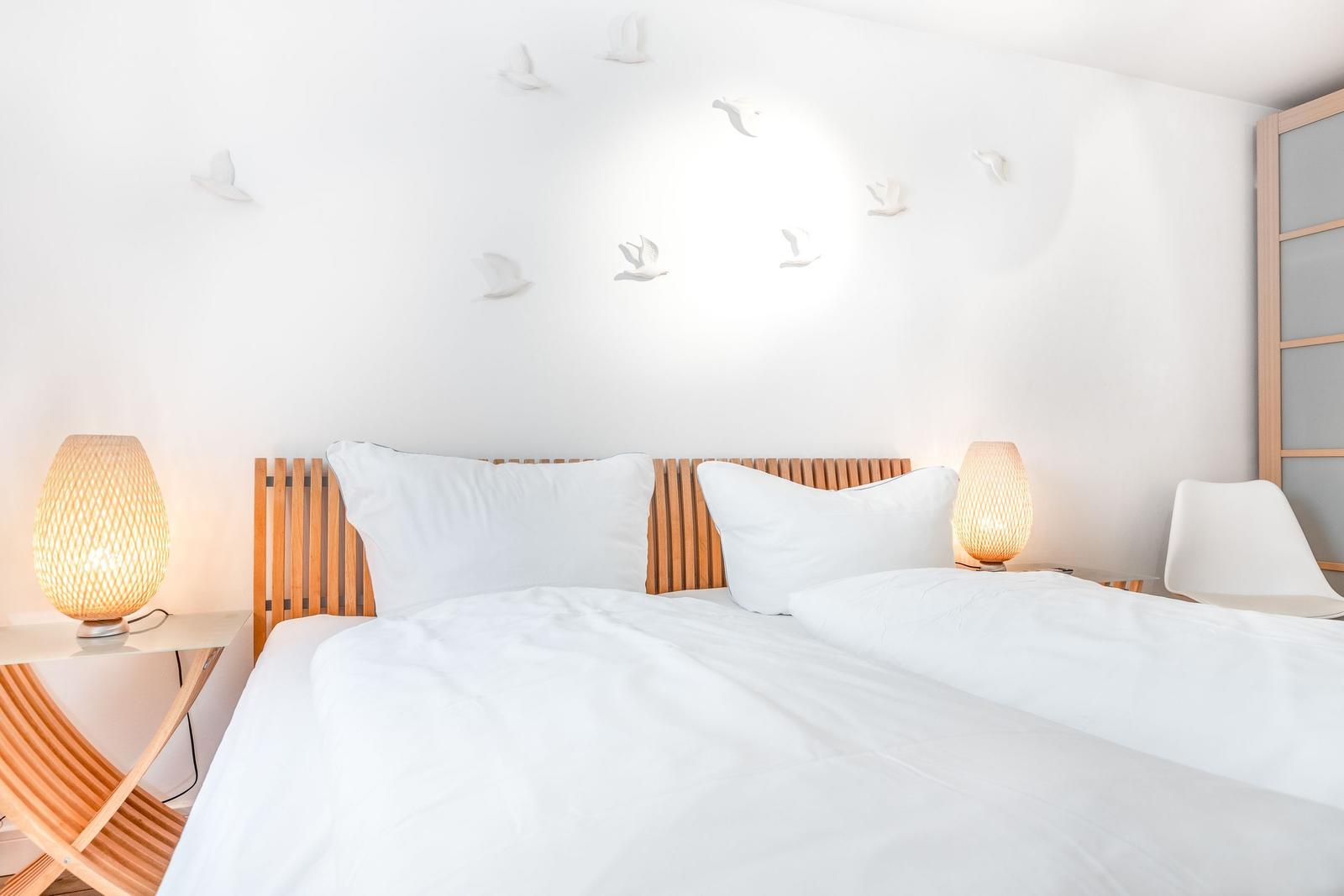 Bedroom with white bedding, wooden headboard, and bird wall decor.