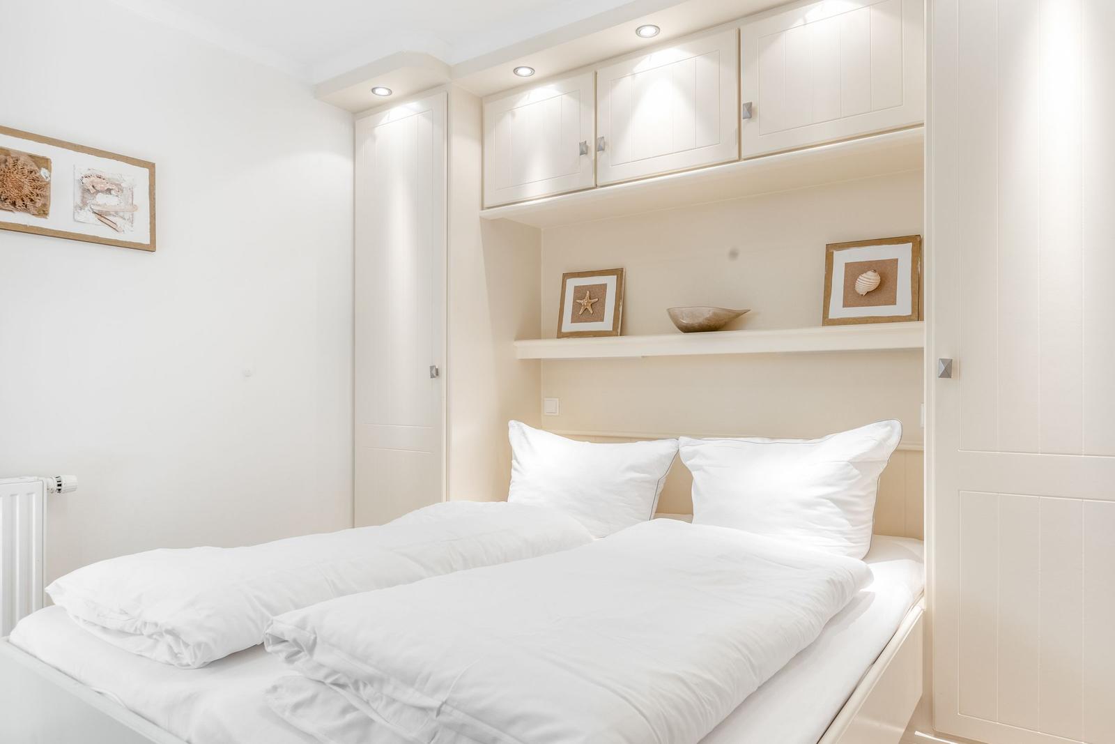 Bedroom with white bed and built-in cabinet above the headboard.