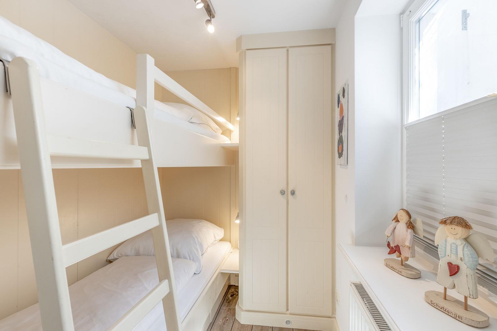 Room with bunk bed, wardrobe, and window with blinds.