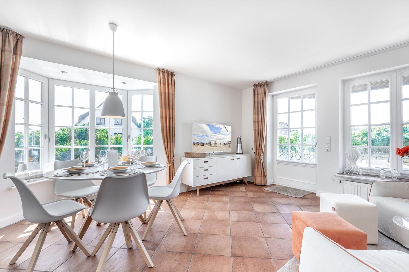 Dining room with table, chairs, and windows. Living area with sofa and TV.