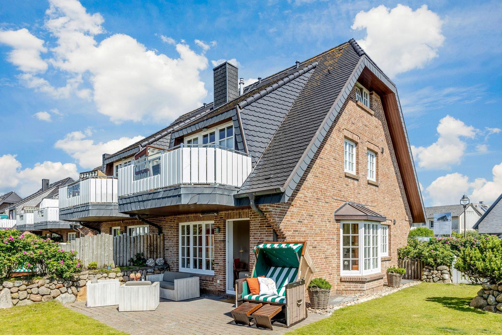 Two-story house with balcony, garden, and beach chair.