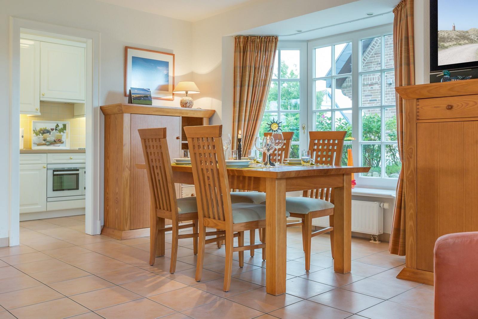 Esszimmer mit Holztisch, Stühlen und Fensterblick. Küche im Hintergrund.