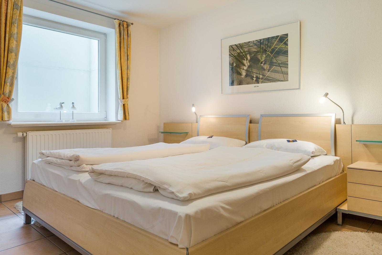 Schlafzimmer mit Doppelbett, Fenster und Nachttischen.