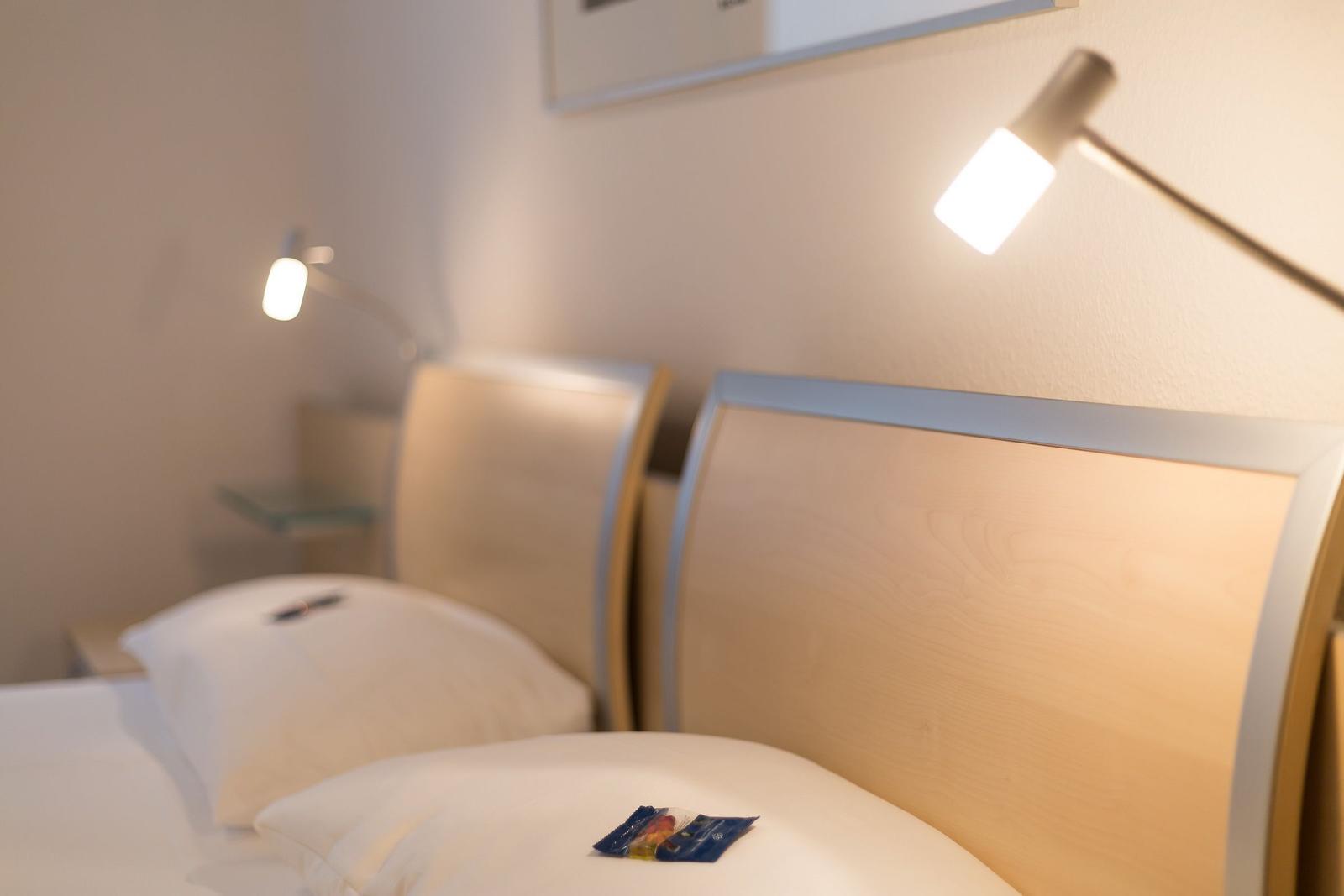 Zwei Betten mit Holz-Kopfteil und Nachttisch mit Lampe.