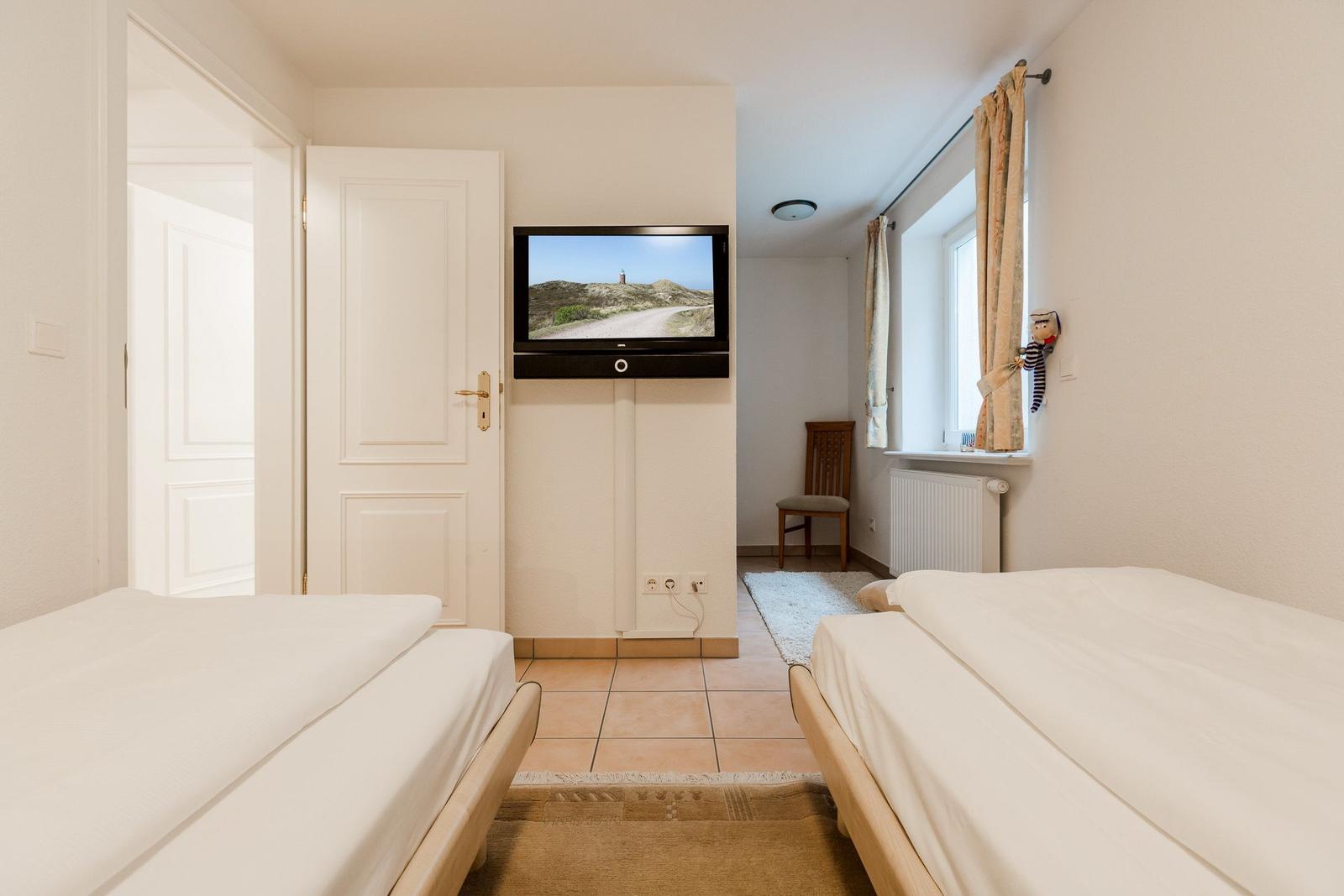 Zwei Betten, Fernseher und Fenster mit Vorhängen.