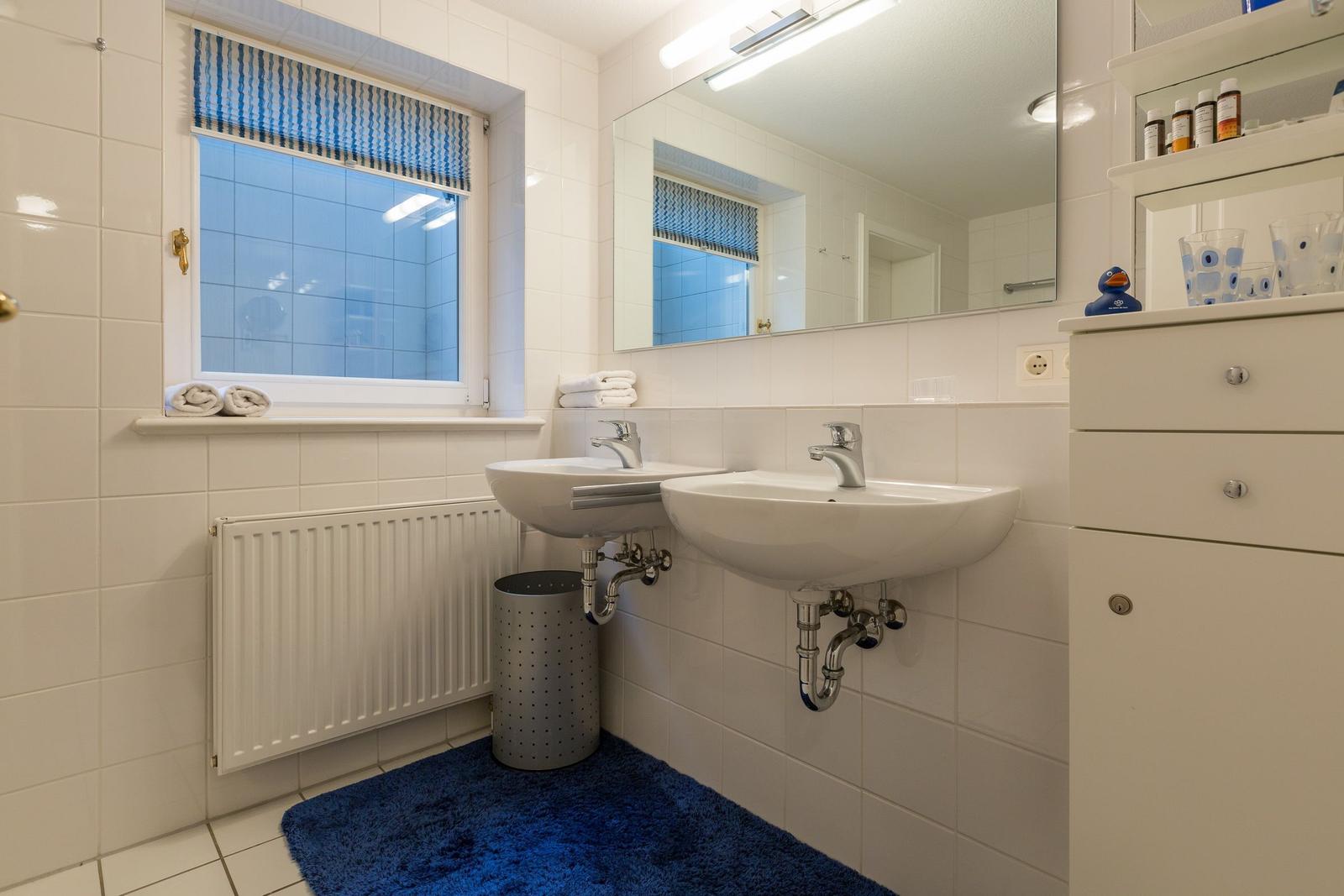 Badezimmer mit zwei Waschbecken, Spiegel und blauem Teppich.