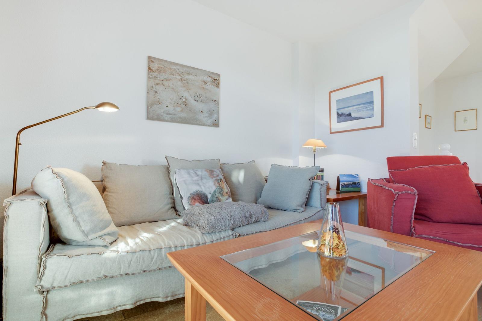 Wohnzimmer mit Sofa, rotem Sessel und Glas-Tisch