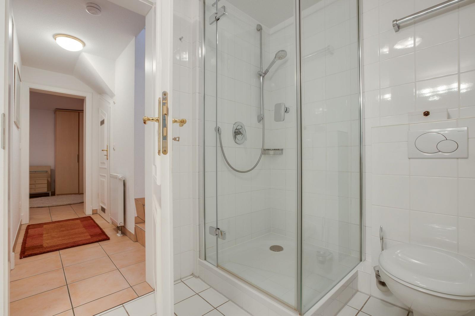 Badezimmer mit Dusche, Toilette und Blick in den Flur.