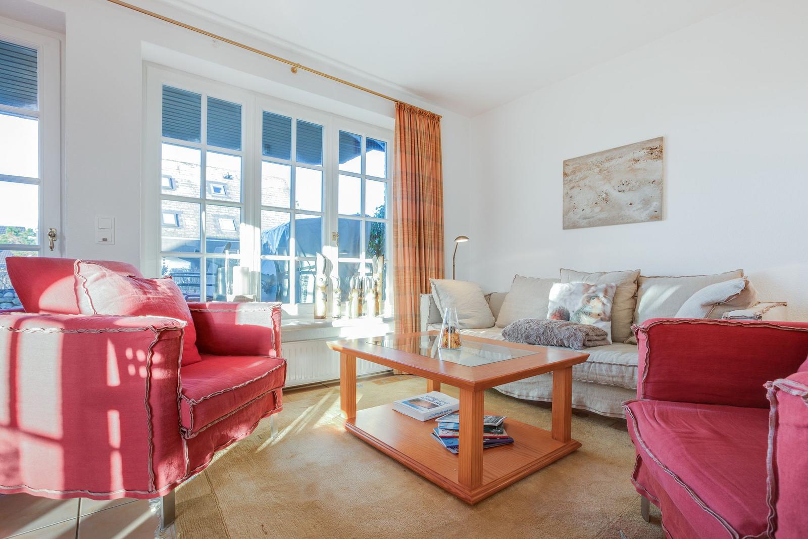 Wohnzimmer mit roten Sesseln, Sofa und Glas-Tisch. Fenster mit Vorhängen.