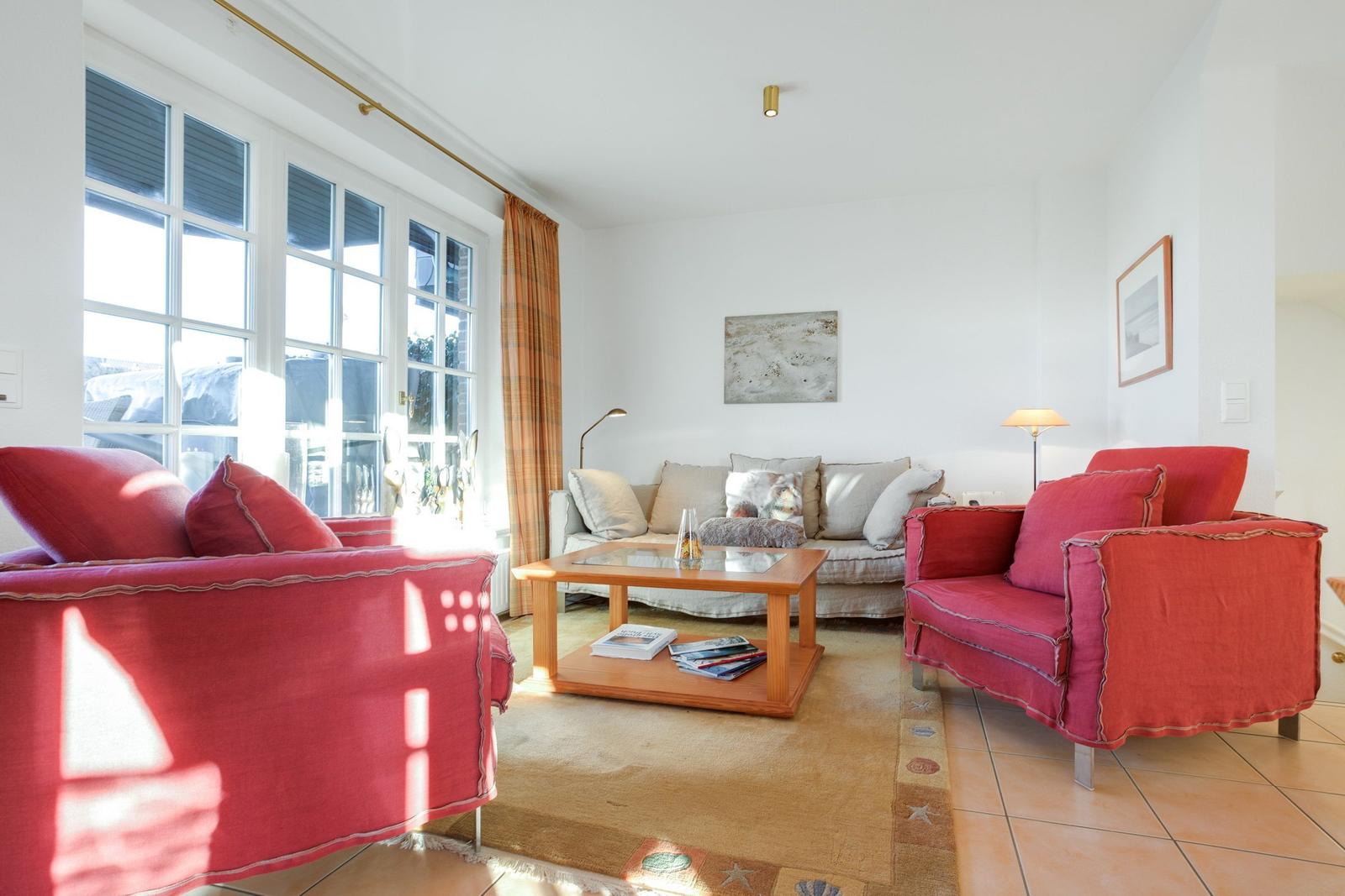 Wohnzimmer mit roten Sesseln, Sofa und Holztisch. Fenster mit Vorhängen.