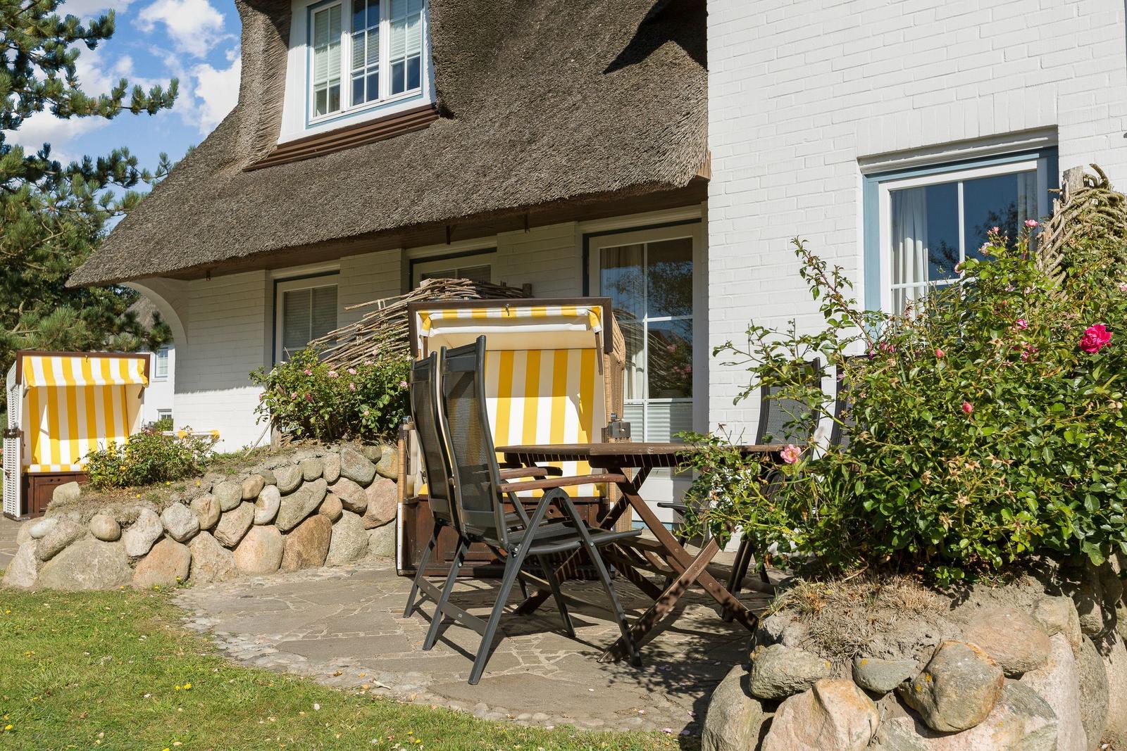 Terrasse mit Tisch, Stühlen und Strandkörben vor einem Haus mit Strohdach.