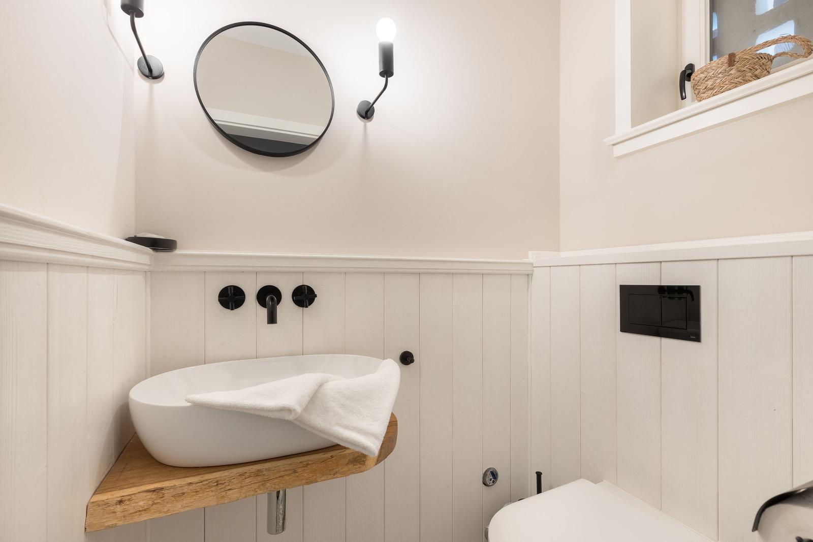 Badezimmer mit Waschbecken auf Holz, Spiegel und Wandbeleuchtung.