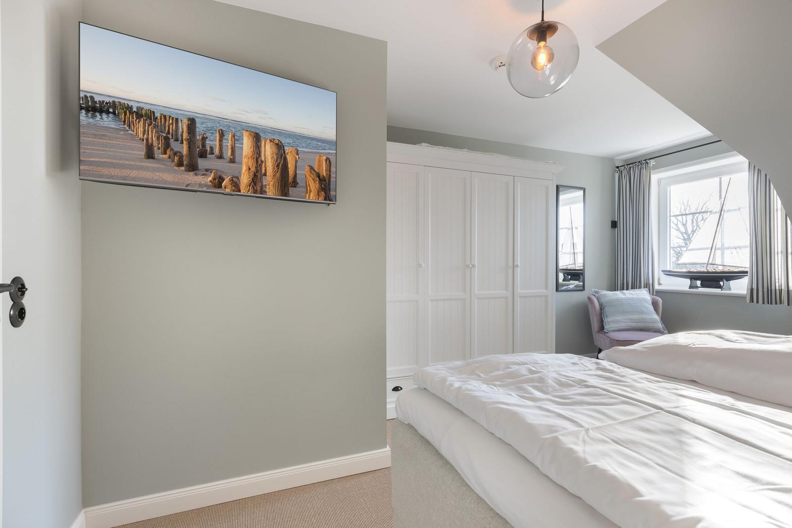 Schlafzimmer mit Bett, Kleiderschrank und TV an der Wand.