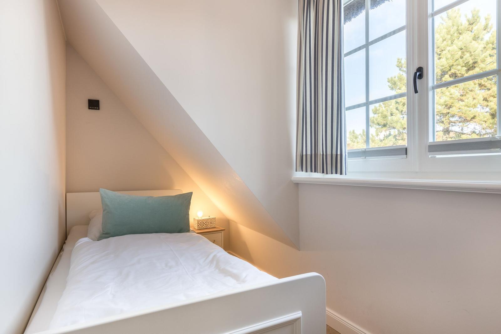 Schlafzimmer mit Dachschräge, Bett und Fenster mit Blick auf Bäume.