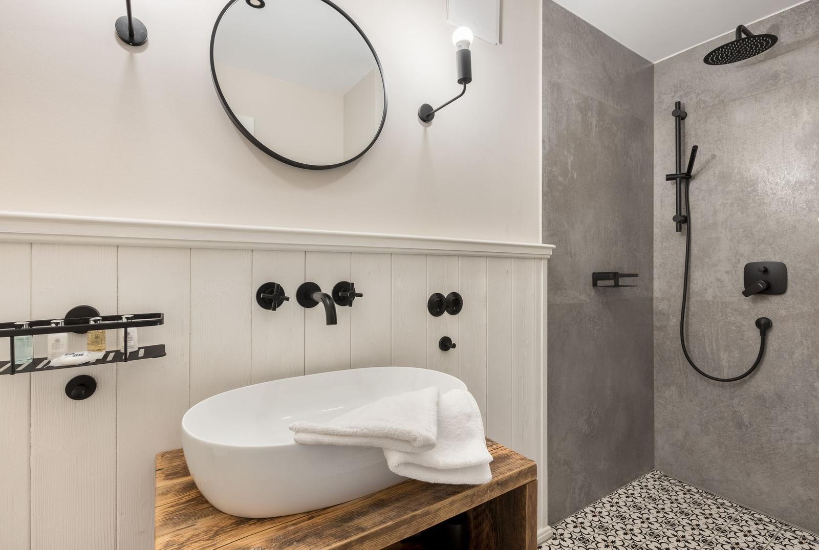 Bad mit Dusche, Waschbecken auf Holz und runden Spiegel.
