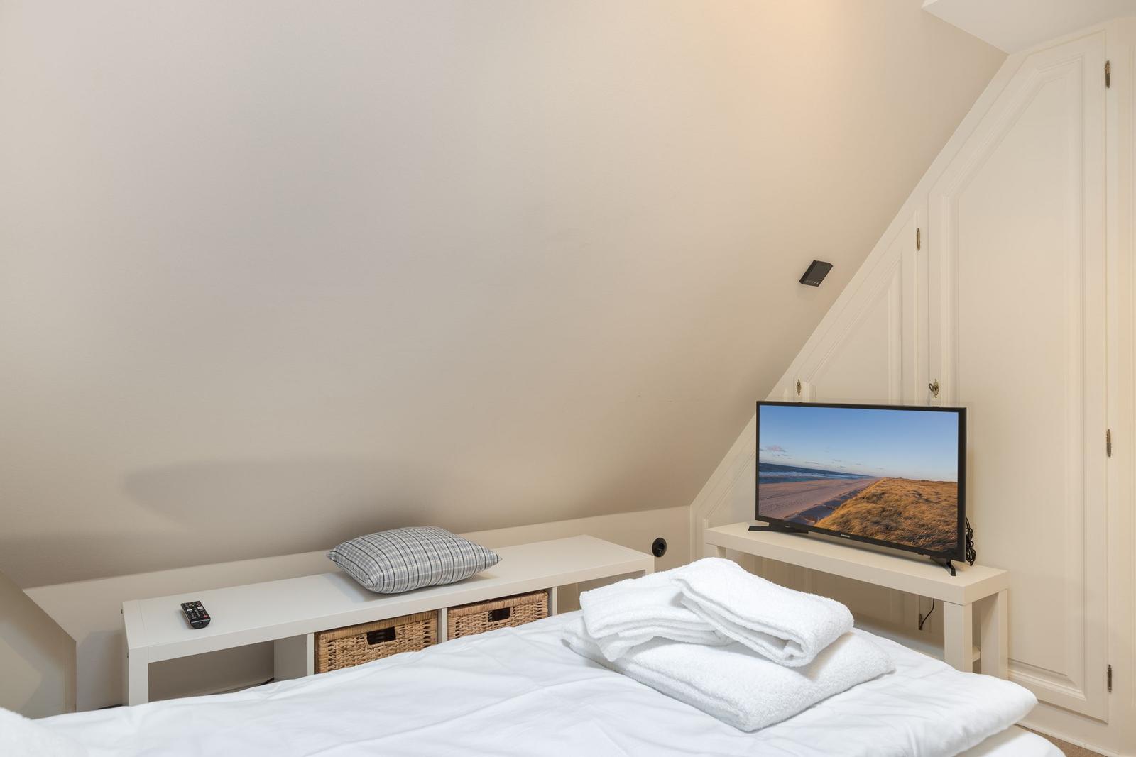 Schlafzimmer mit Bett, Fernseher und Kleiderschrank unter Dachschrägen.