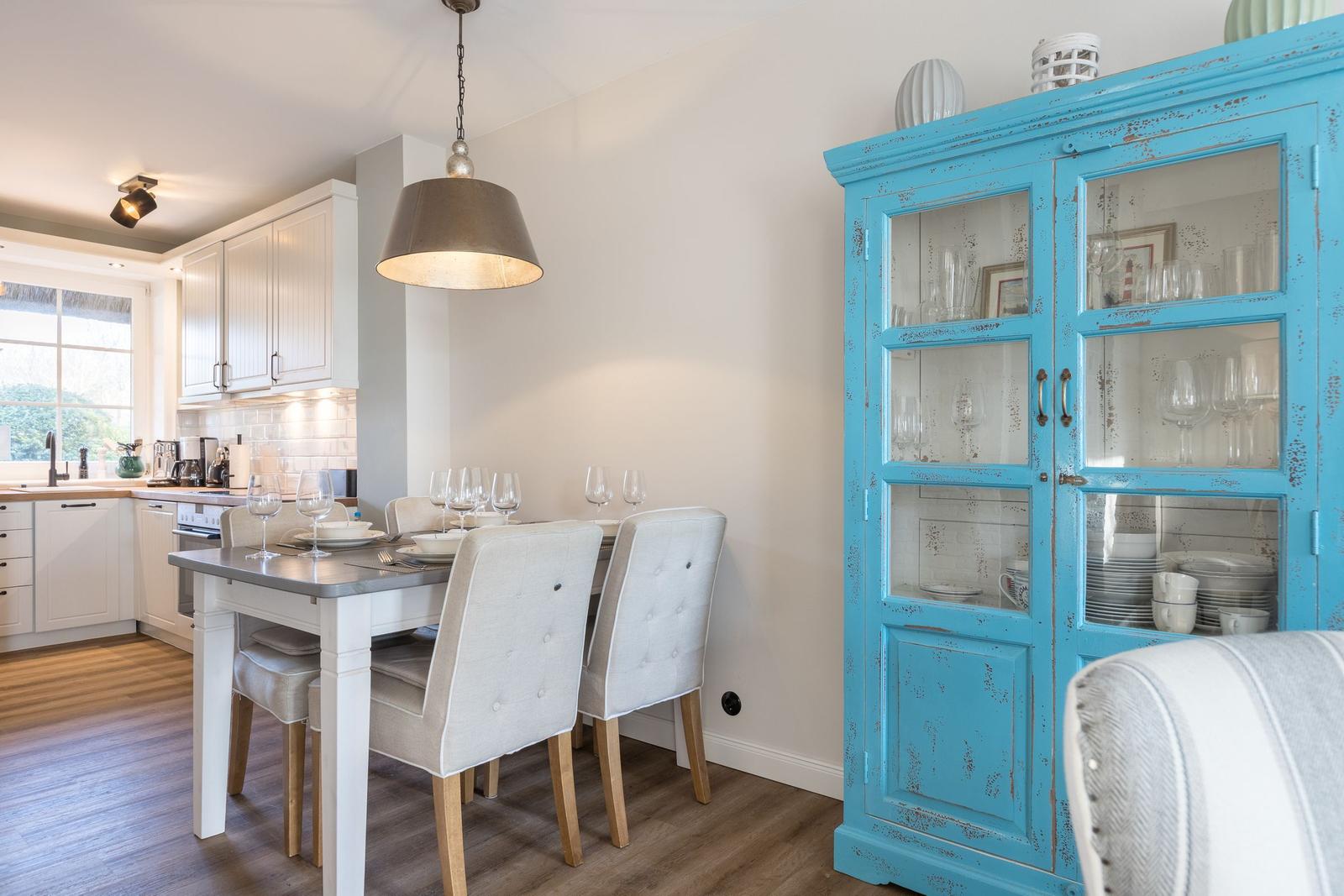 Essbereich mit Tisch, Stühlen und blauem Schrank. Küche im Hintergrund.