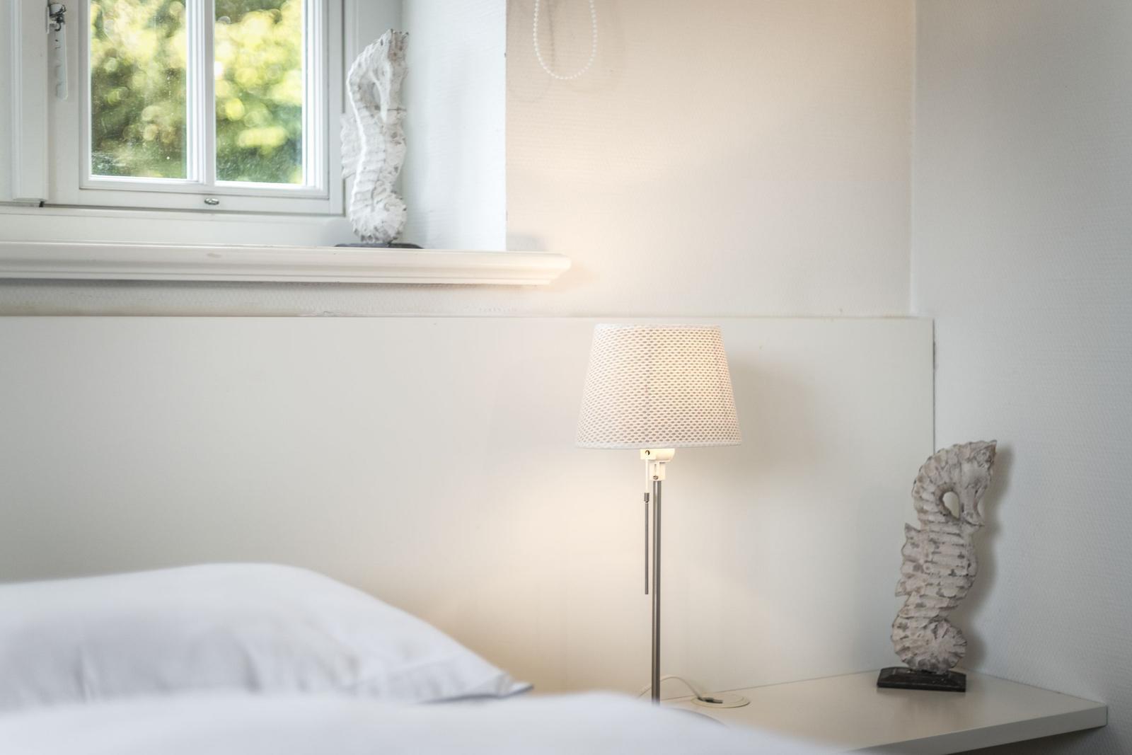 Schlafzimmer mit Bett, Stehlampe und Fenster mit Blick auf Grün.