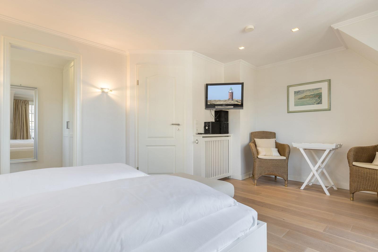 Schlafzimmer mit Bett, Fernseher und zwei Stühlen.