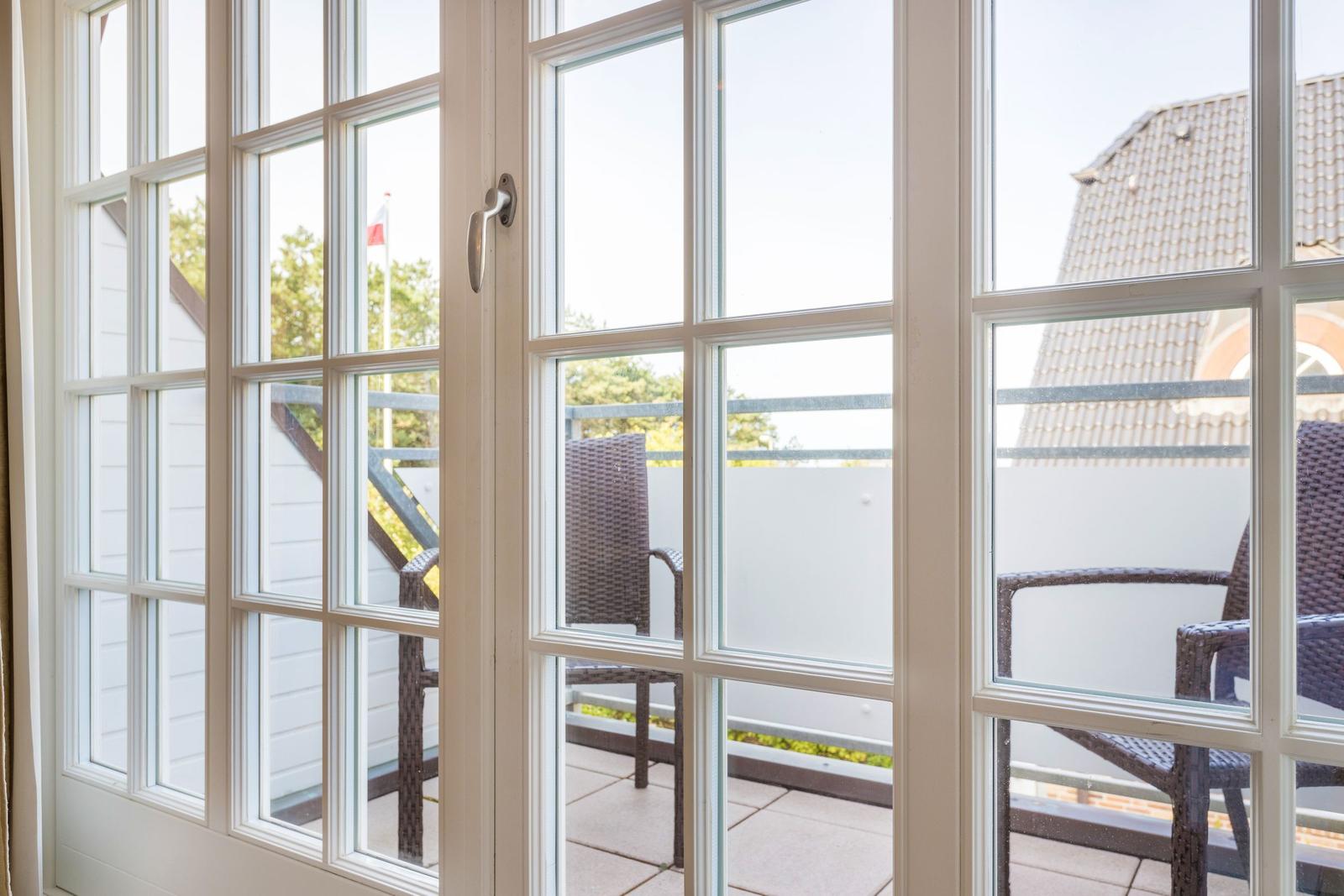 Durch die Glastüren ist eine Terrasse mit Stühlen und Blick auf ein Haus sichtbar.