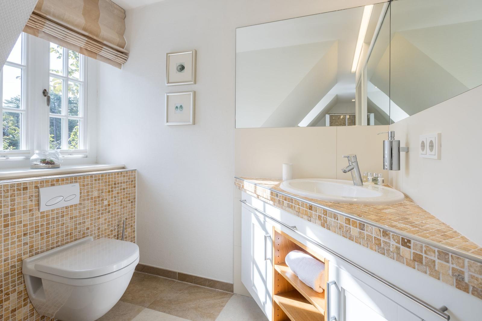 Badezimmer mit Waschbecken, Spiegel und Toilette. Fenster mit Blick nach draußen.