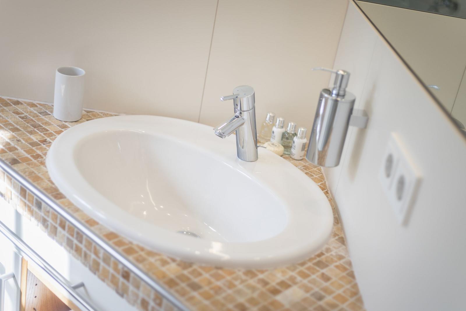 Waschbecken mit Chromhahn und Seifenspender auf Mosaik-Arbeitsplatte