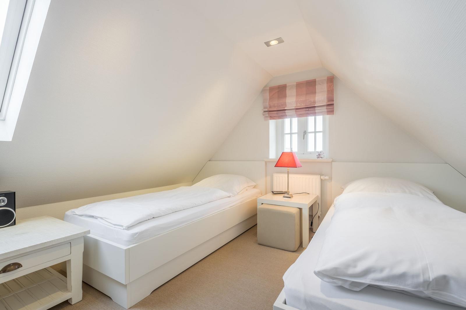 Zwei Betten mit weißen Laken, Nachttisch mit Lampe und Fenster mit Rollladen.