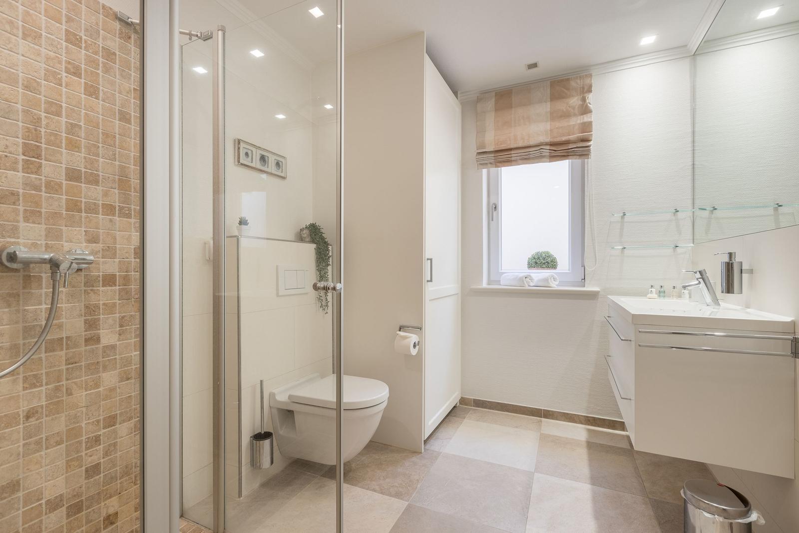Badezimmer mit Dusche, WC und Waschbecken. Fenster mit Rollladen und Pflanze.