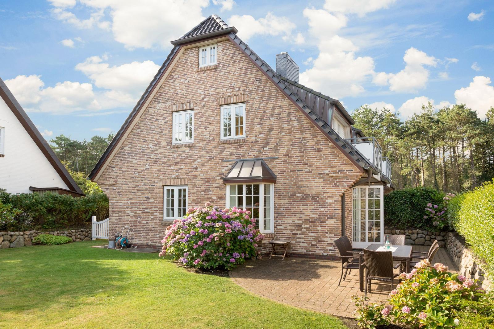 Haus mit Steinmauer, Terrasse und Blumenbeete im Garten