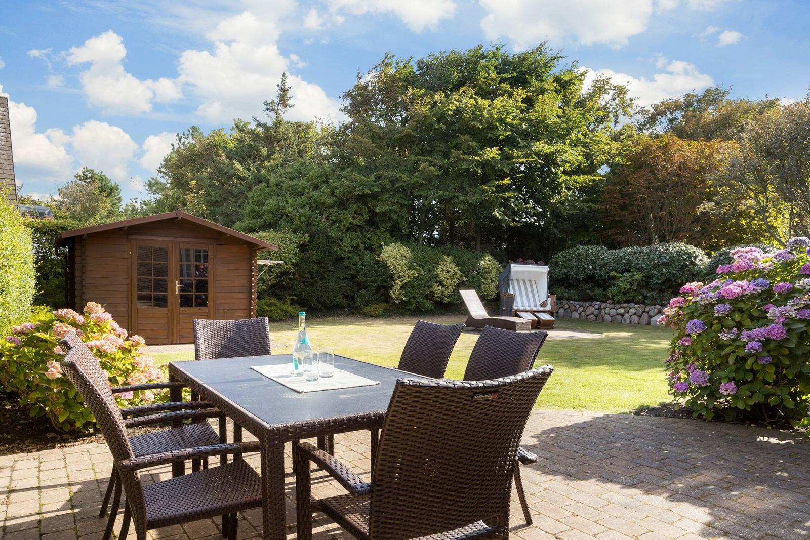 Garten mit Tisch, Stühlen, Holzhaus und Blumen.